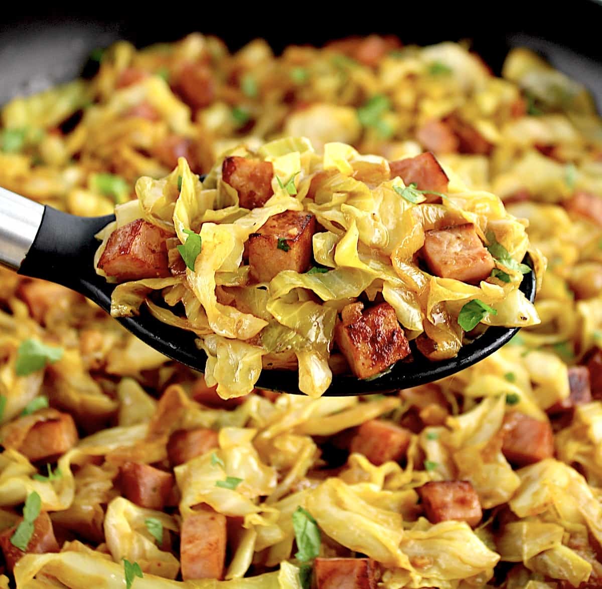 Fried Cabbage with Ham being held up by serving spoon