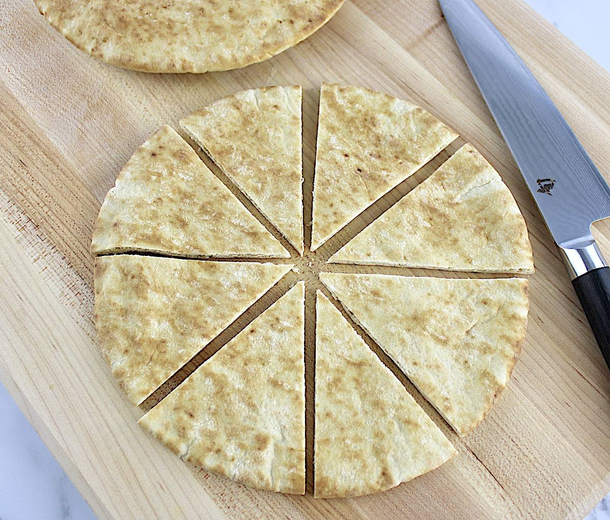 pita bread cut into 8 triangles with knife on cutting board