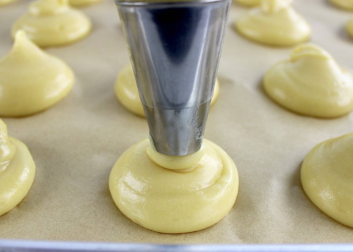 cream puff dough being piped onto parchment paper