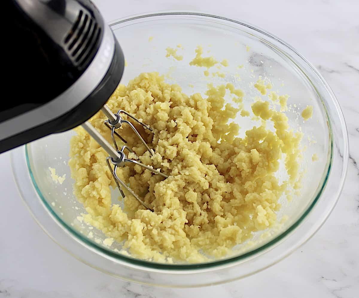 cream puff dough in glass bowl being mixed with hand mixer