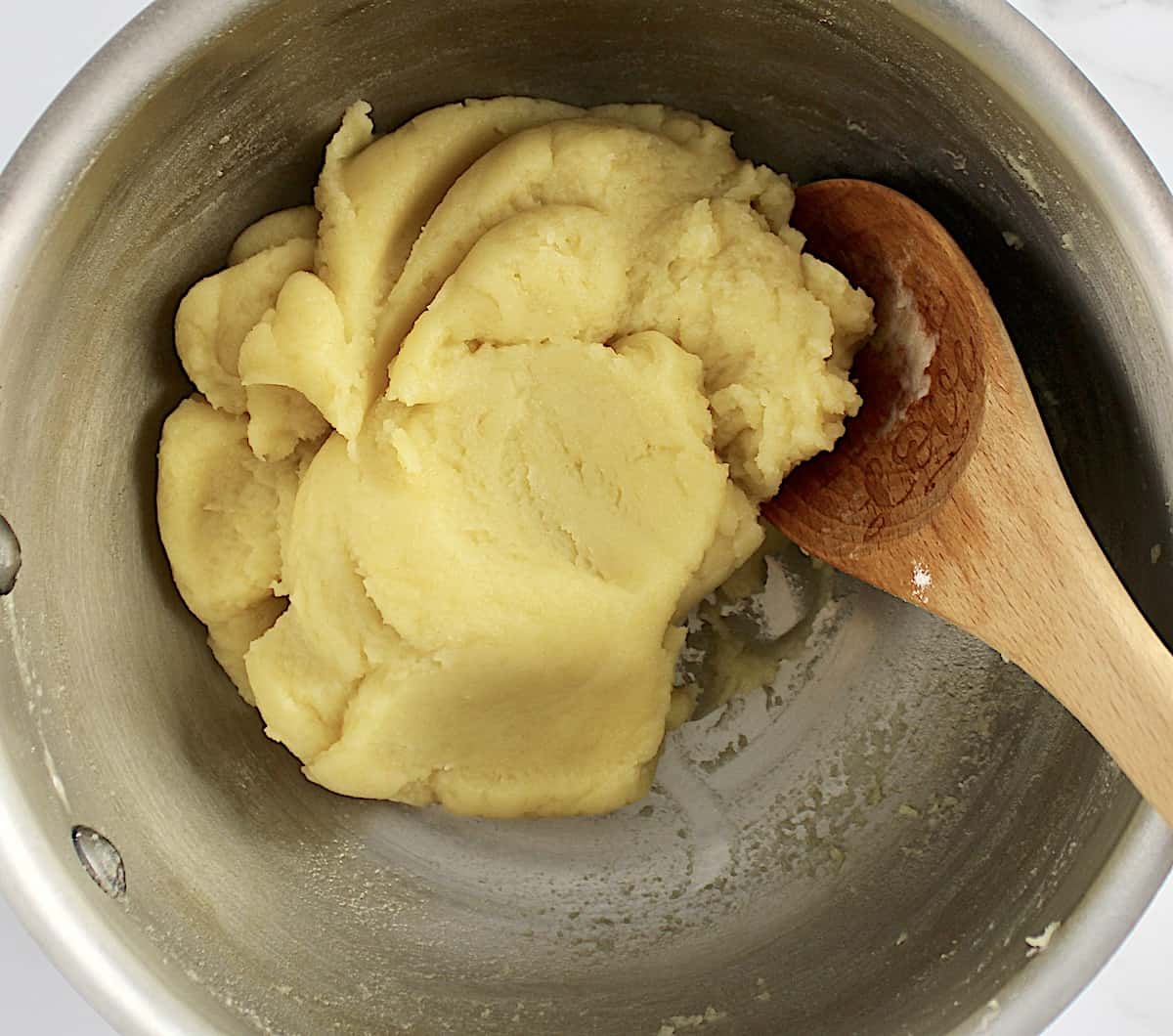 cream puff dough in saucepan with wooden spoon