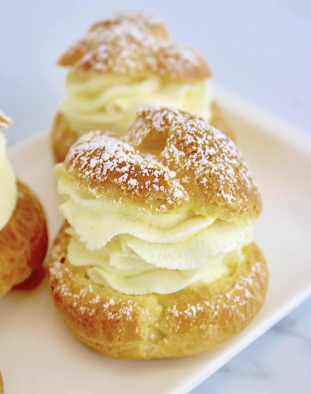 closeup of Lemon Cream Puffs on white plate with powdered sugar on top
