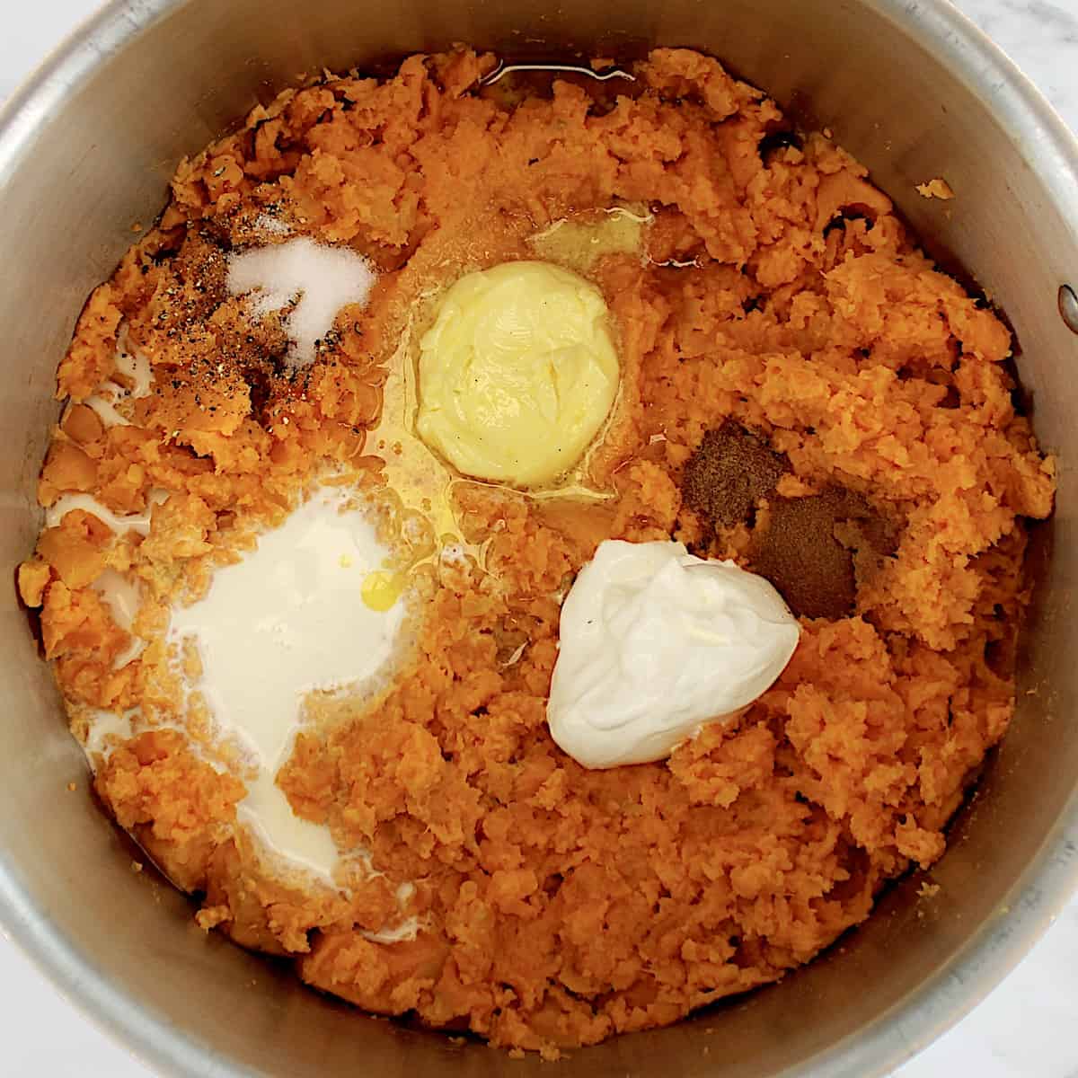 Mashed Sweet Potatoes with butter, sour cream, maple syrup, spices and cream in pot unmixed