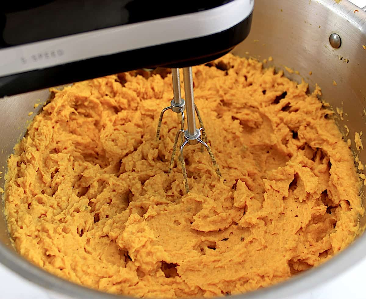 sweet potatoes in pot being whipped with hand mixer