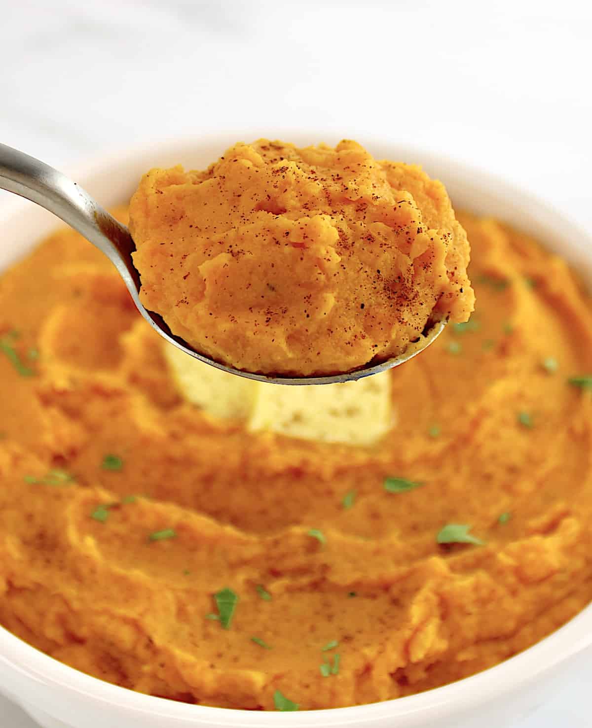 Mashed Sweet Potatoes in spoon held up over bowl