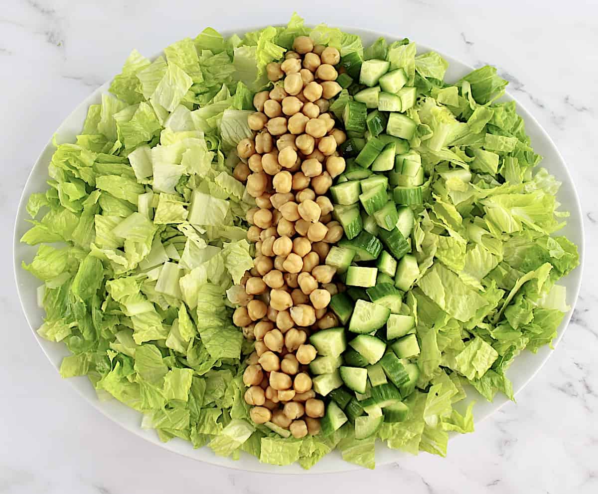 chopped lettuce in white oval platter with chickpeas and chopped cucumber down the center