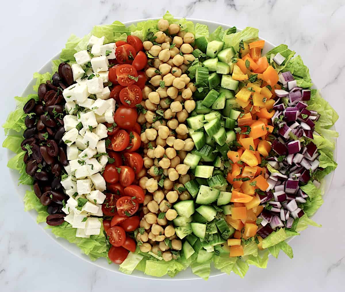 Mediterranean Chopped Salad in oval white platter with veggies arranged in rows 
