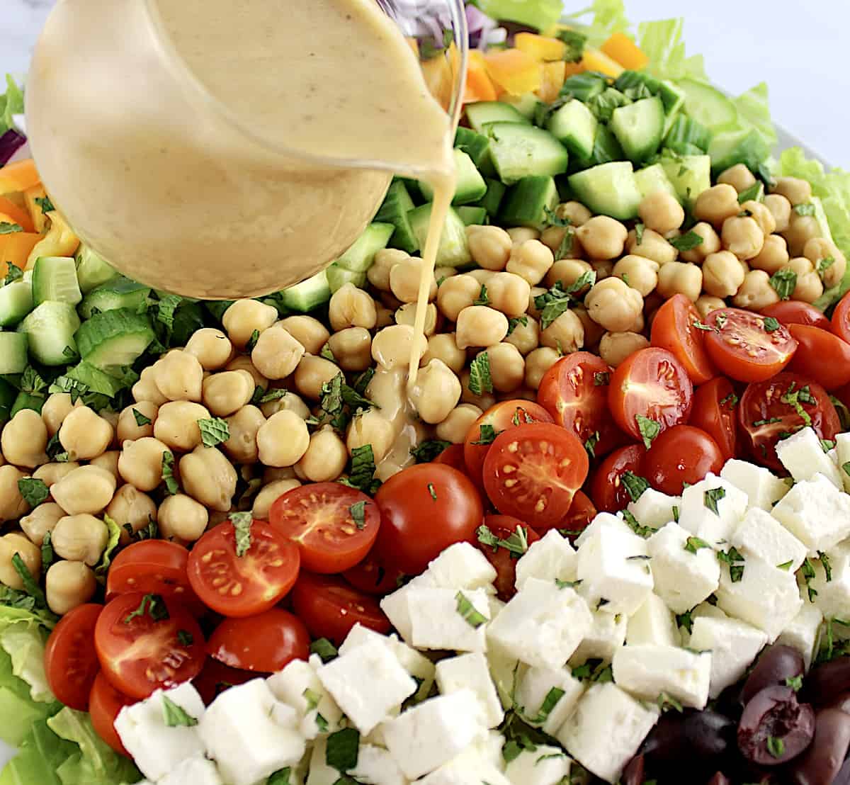 Mediterranean Chopped Salad with veggies arranged in row and dressing being poured over top