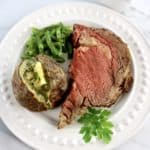 Prime Rib on white plate with baked potato and green beans