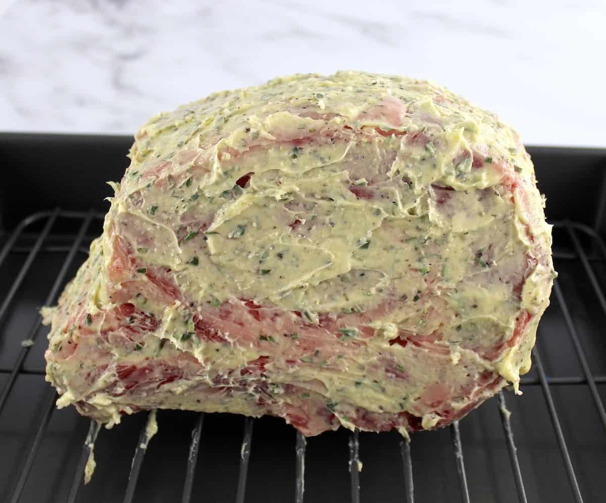 herbed butter covered raw prime rib in roasting pan on wire rack