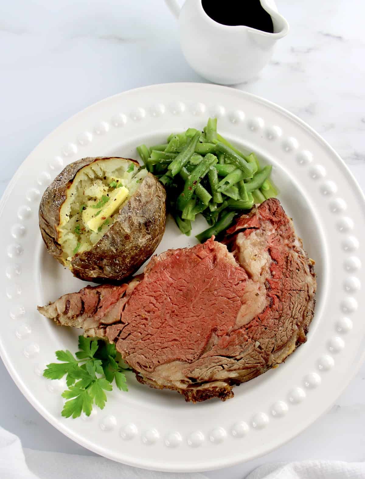 Prime Rib on white plate with baked potato and green beans