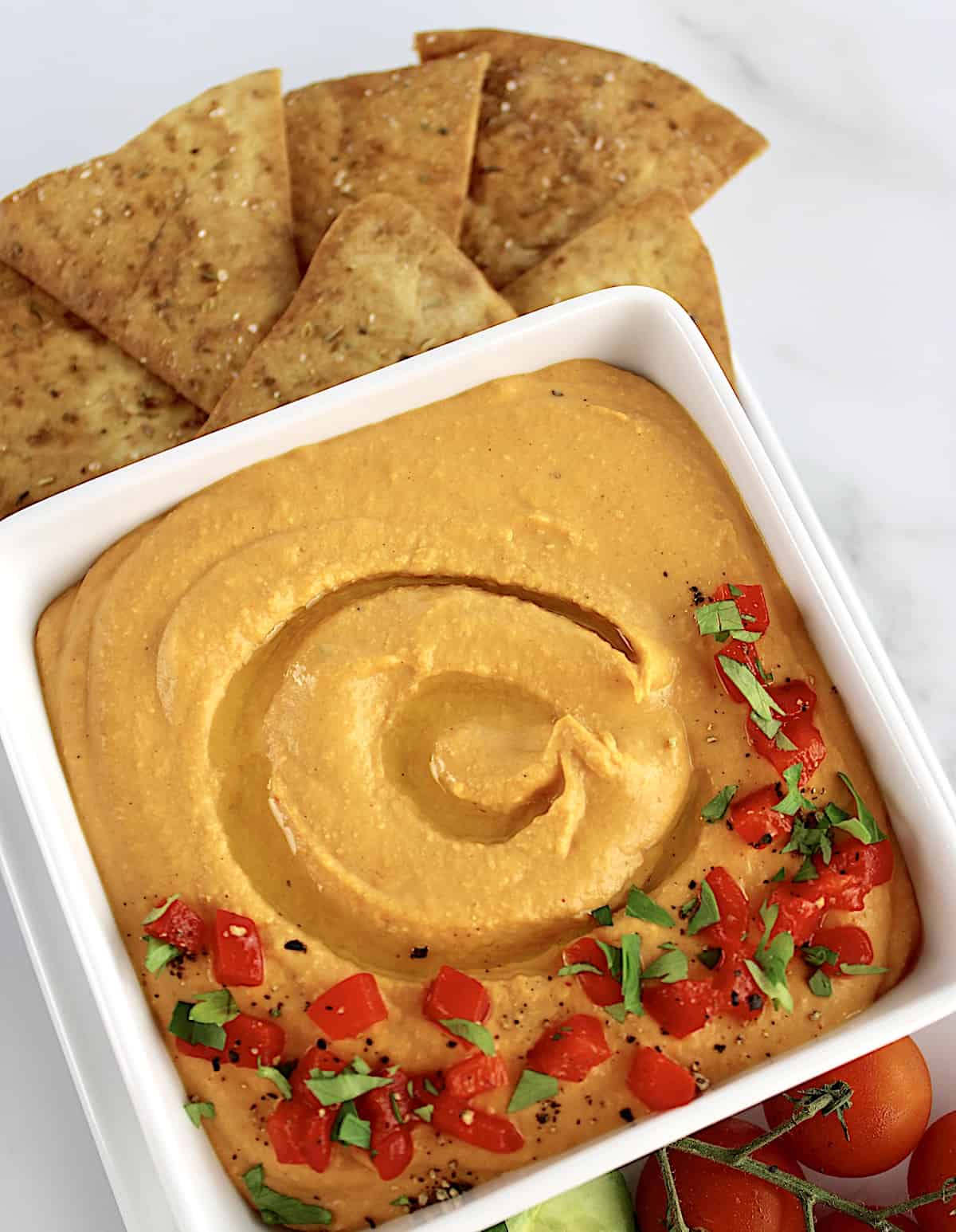 Roasted Red Pepper Hummus in white square bowl with pita chips on side