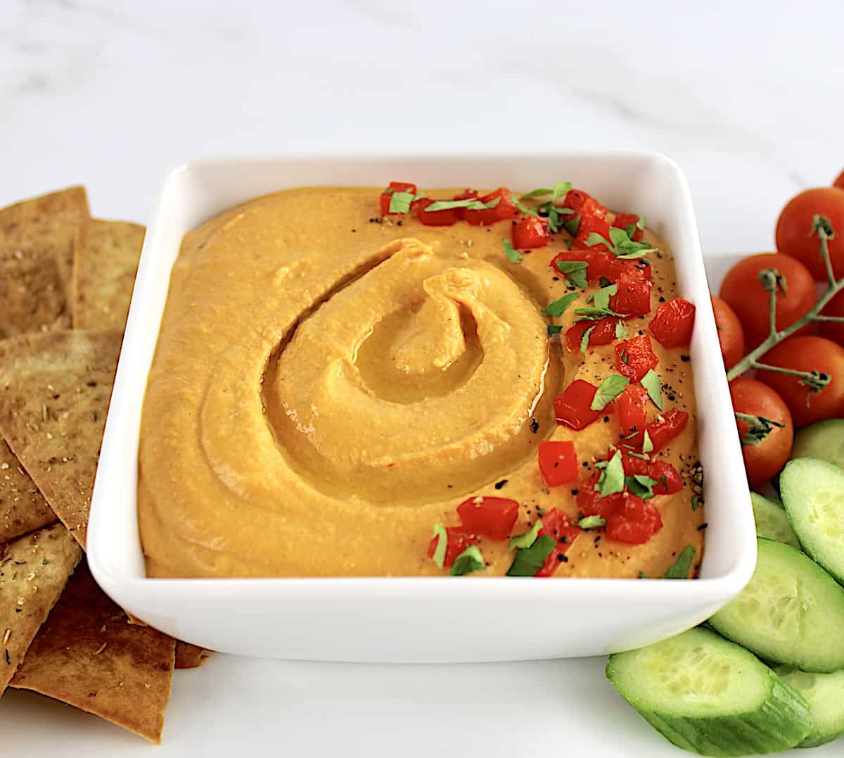 Roasted Red Pepper Hummus in white square bowl with chopped peppers on top