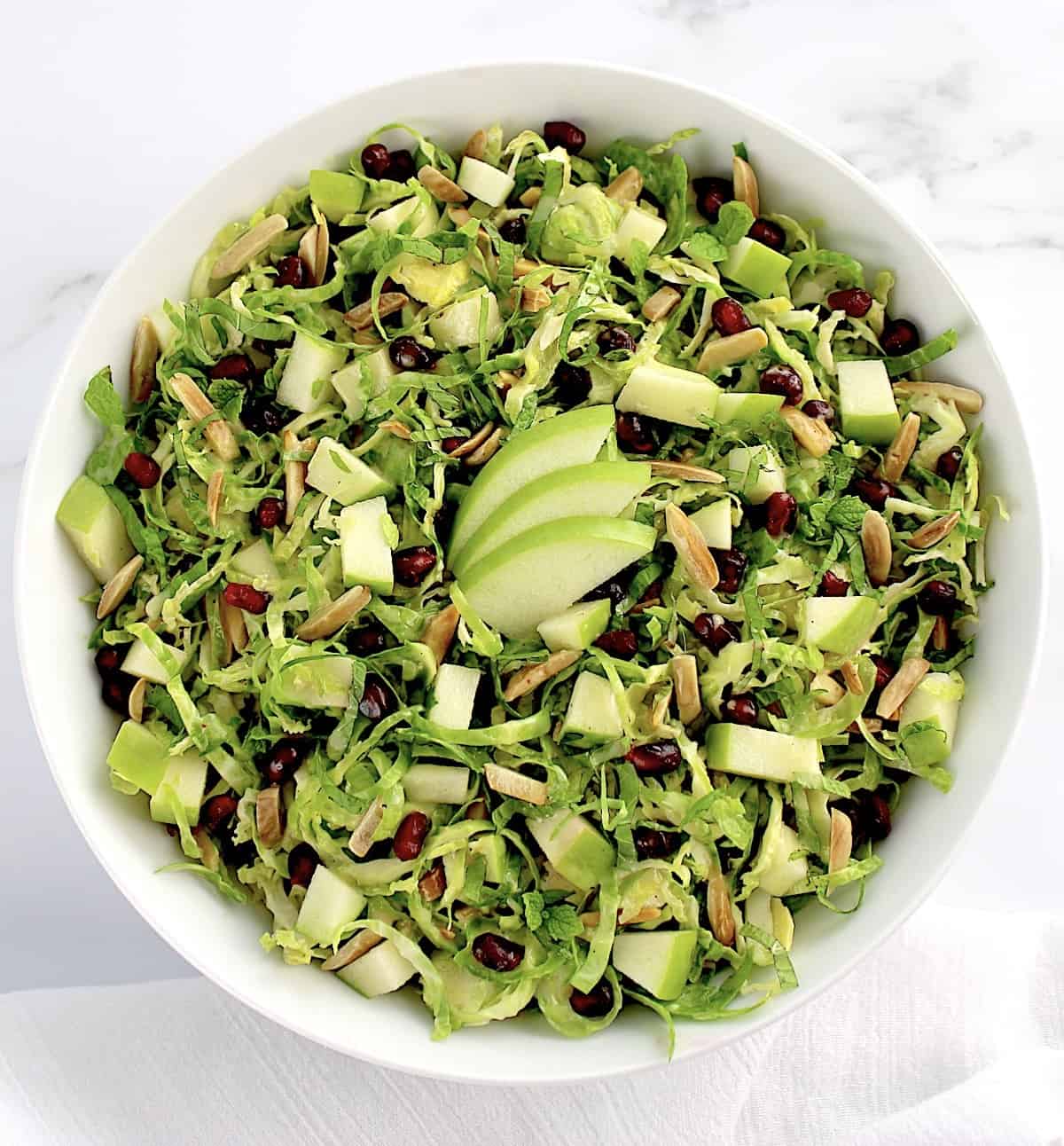 overhead view of Shredded Brussels Sprouts Salad in white bowl with 3 sliced of green apple on top