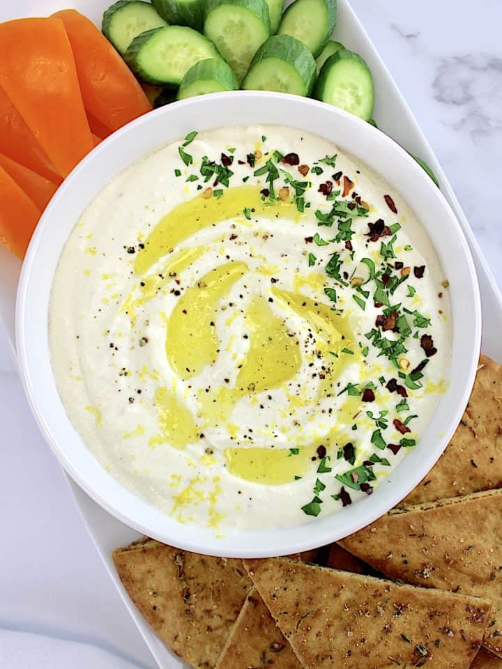 Whipped Feta Dip in white bowl with pita chips, cucumber. slices and orange pepper strips on side