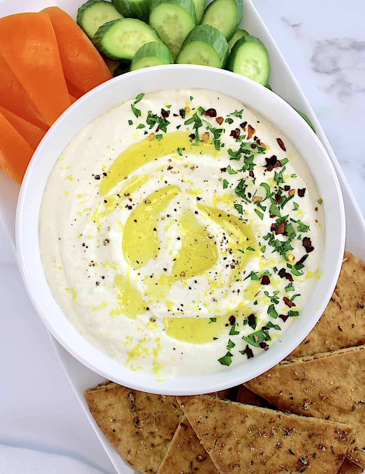 Whipped Feta Dip in white bowl with pita chips, cucumber. slices and orange pepper strips on side