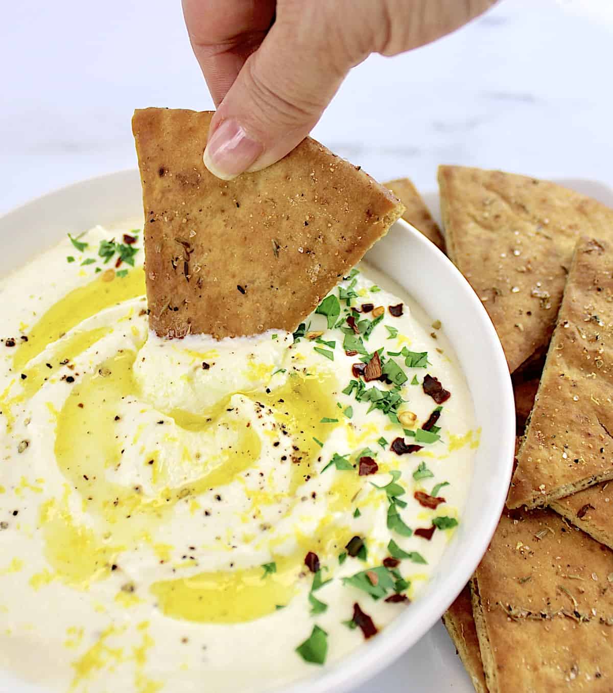 pita chip being dipped into whipped feta dip in white bowl