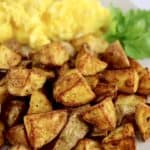 Air Fryer Home Fries on white plate with scrambled eggs and parsley garnish