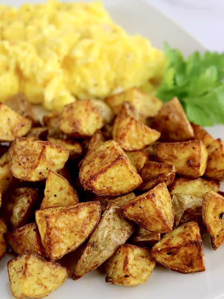 Air Fryer Home Fries on white plate with scrambled eggs and parsley garnish