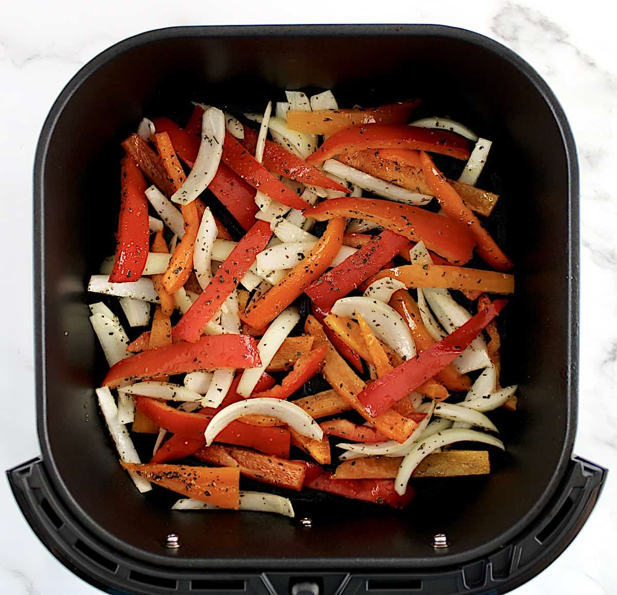 red and orange bell pepper and onion slices in air fryer basket