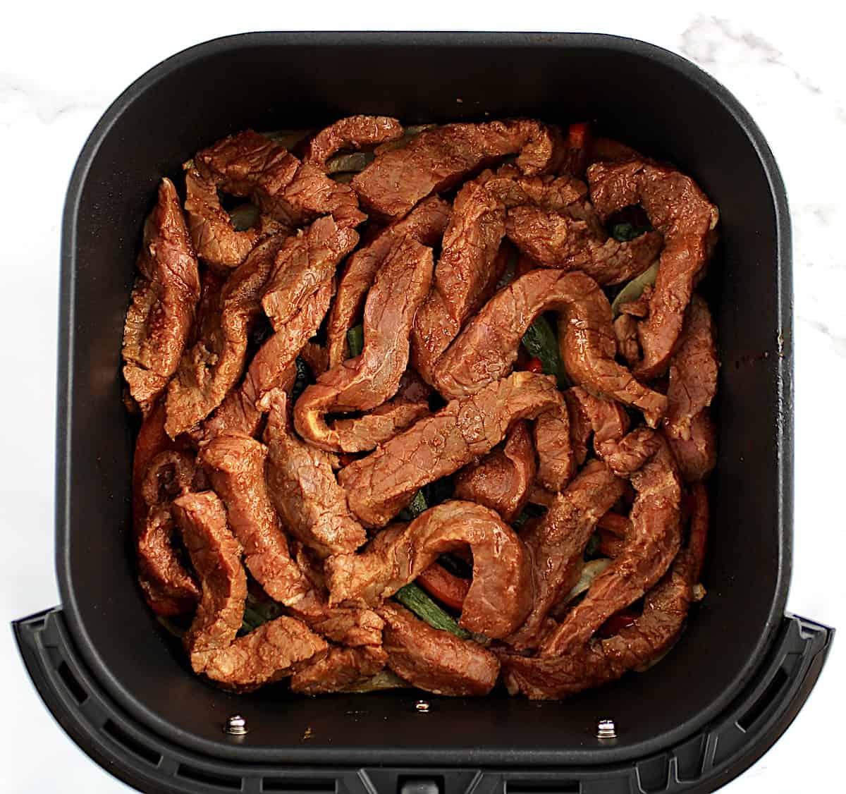 fajita seasoned steak strips uncooked in air fryer basket