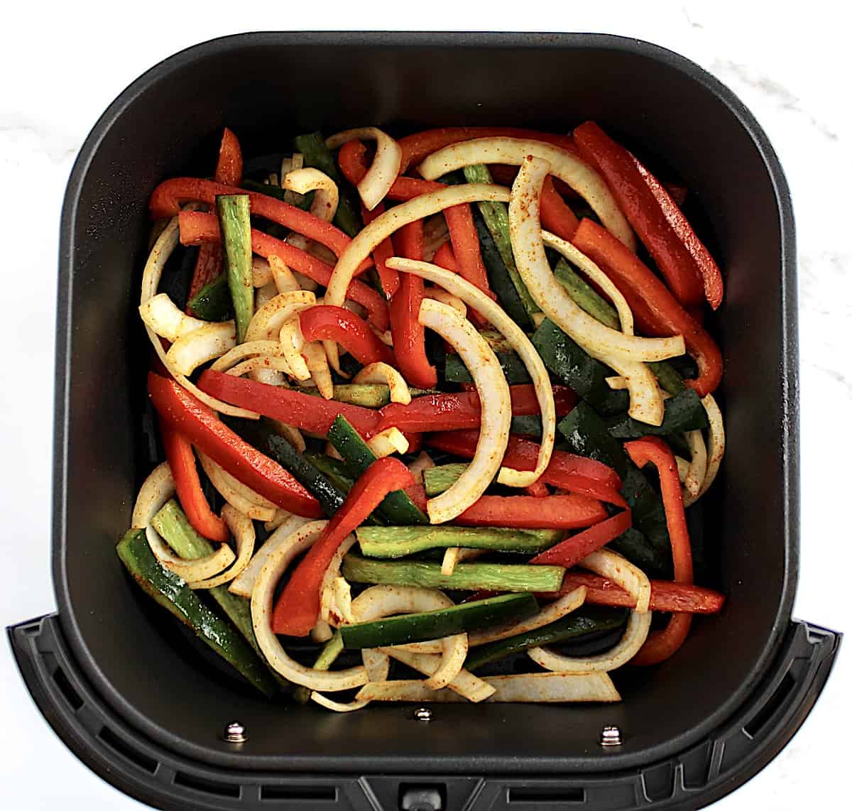 sliced onions, red and green peppers with fajita seasoning in air fryer basket