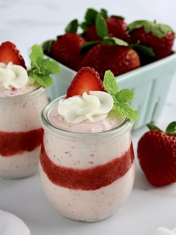 Easy Strawberry Mousse in 2 glass jars with whip cream and strawberry slice on top