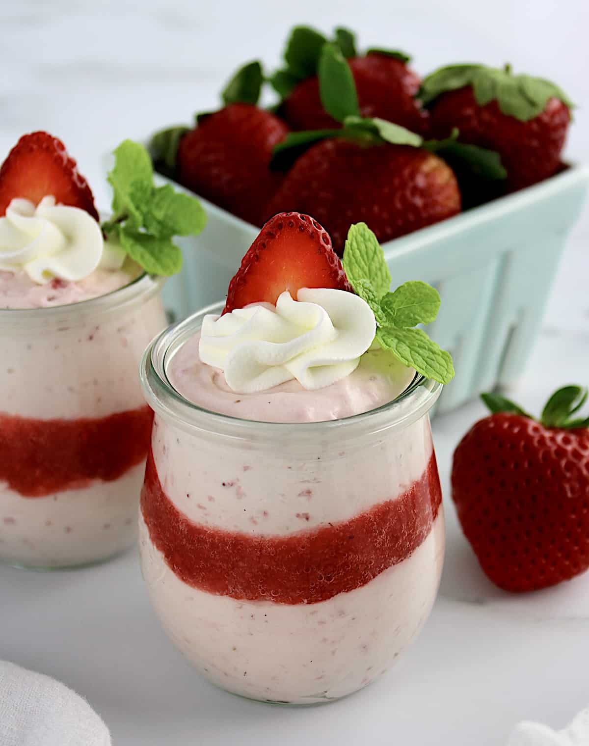 Easy Strawberry Mousse in 2 glass jars with whip cream and strawberry slice on top