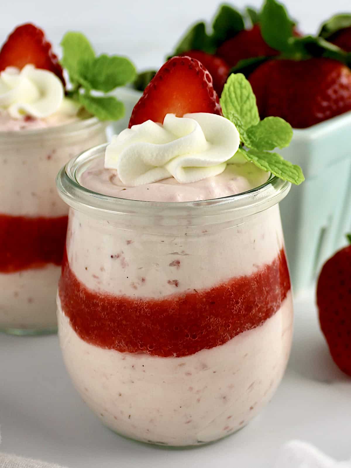 side view of Easy Strawberry Mousse in 2 glass jars with whip cream and strawberry slice on top