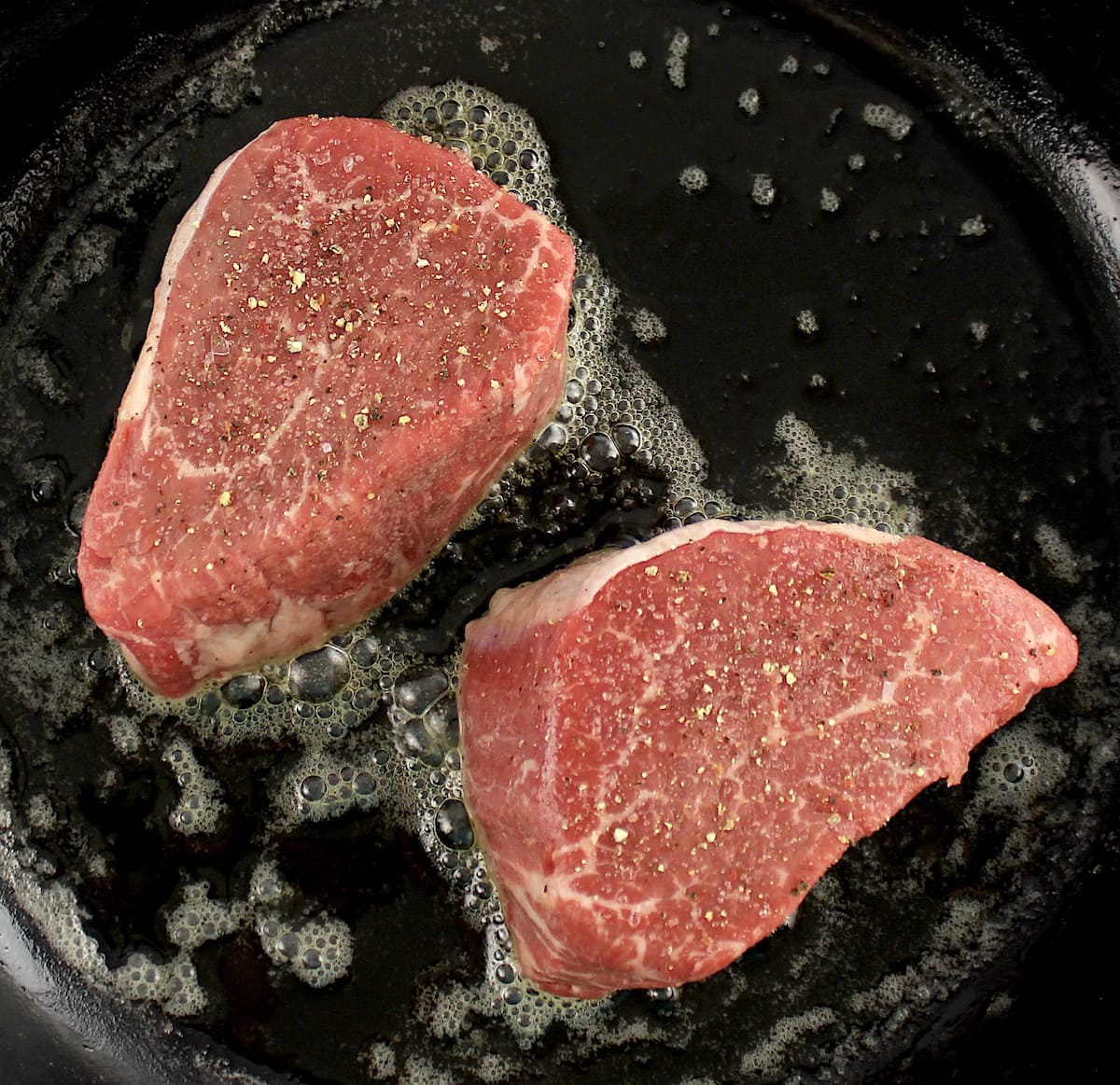 2 filet mignon steaks in skillet cooking