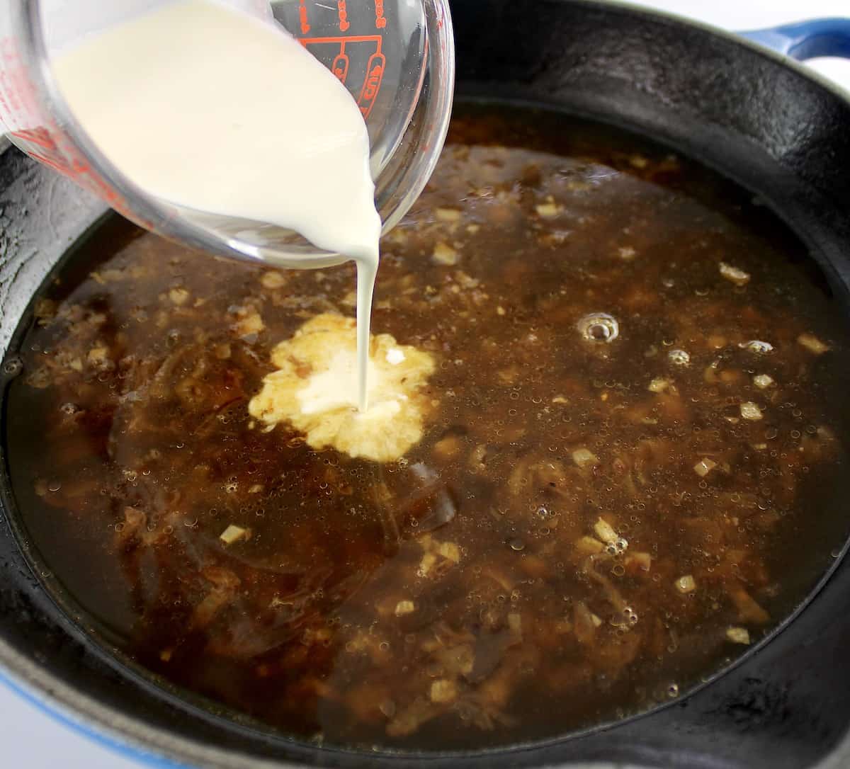 beef broth in skillet with heavy cream being poured in
