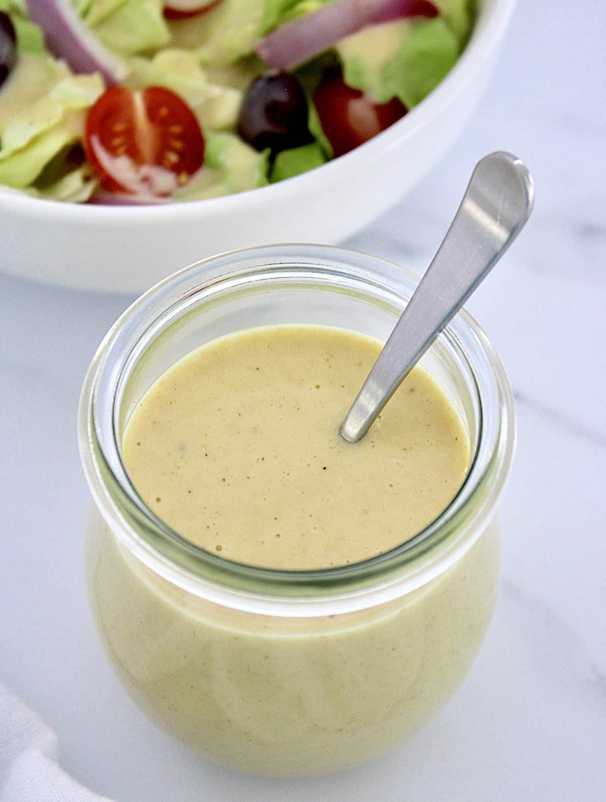 closeup of Honey Mustard Dressing in open jar with spoon in it and salad in background