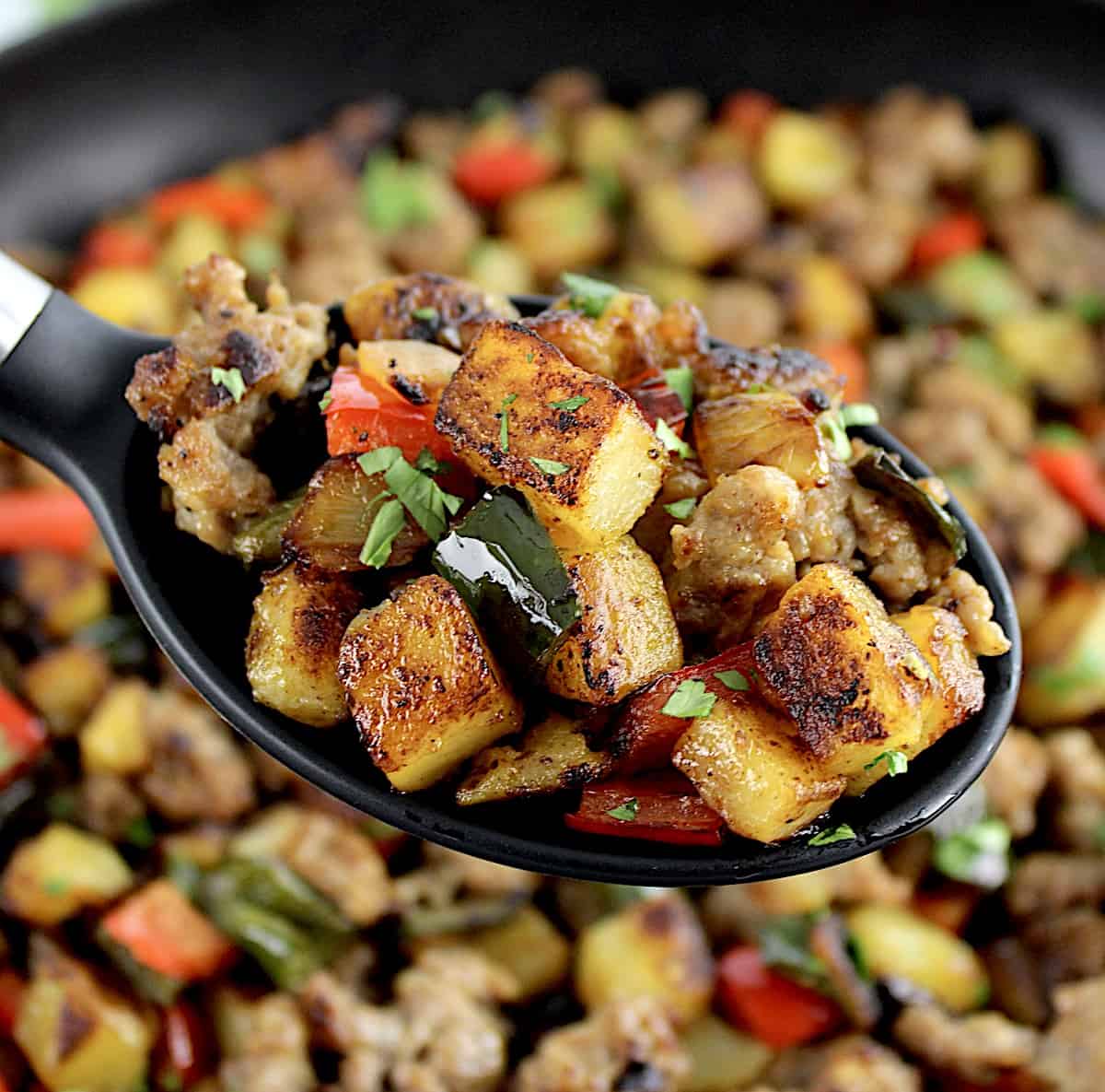 Italian Sausage and Peppers Hash in black serving spoon over skillet