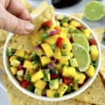 tortilla chip being dipped into Mango Salsa in white bowl with tortilla chips around