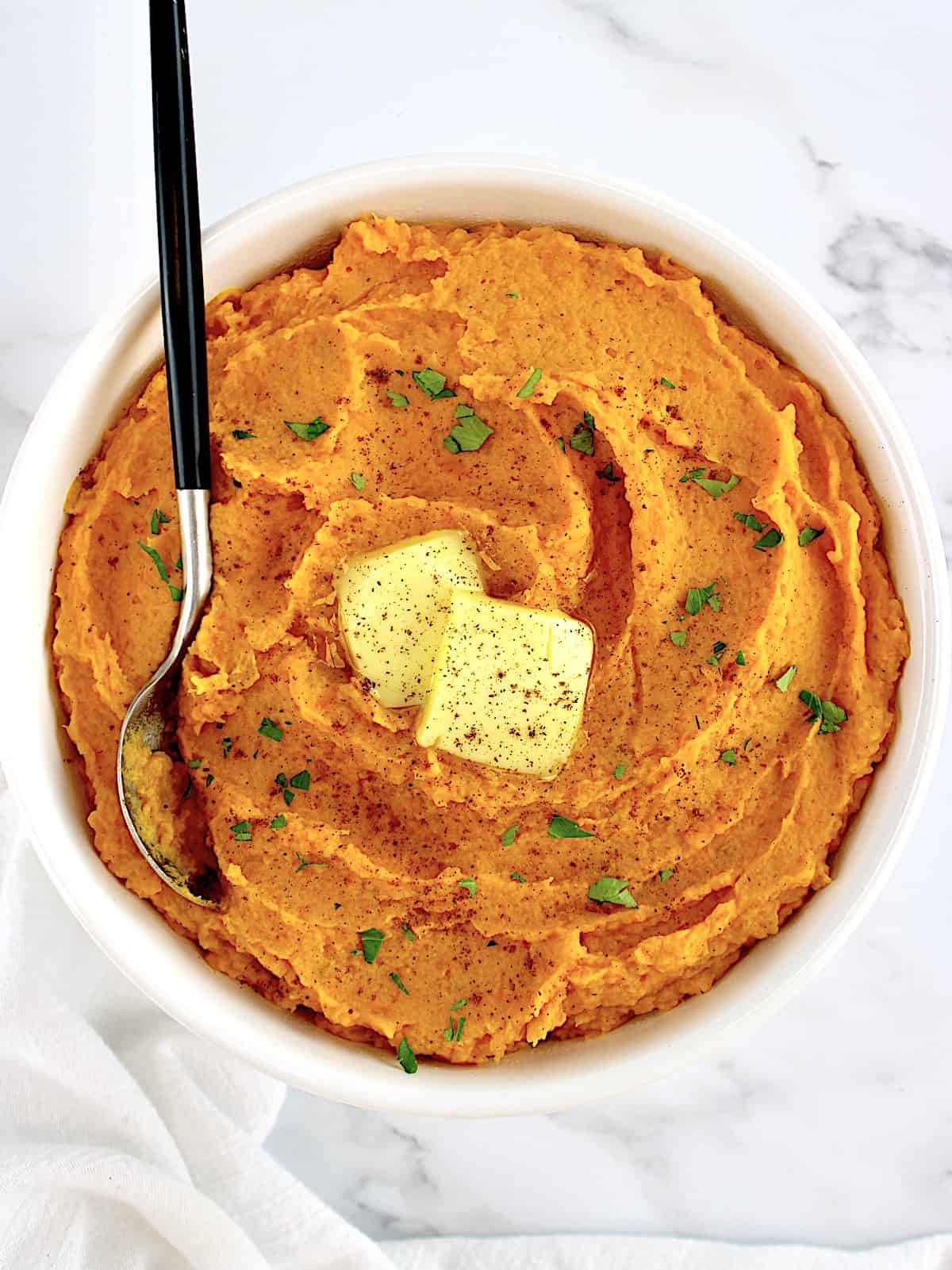 Mashed Sweet Potatoes in white bowl with 2 pats of butter and spoon inn bowl
