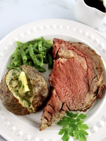 Prime Rib on white plate with baked potato and green beans