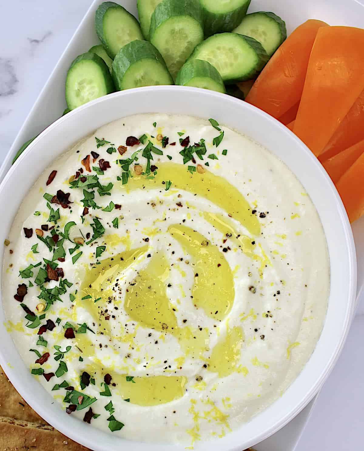 Whipped Feta Dip in white bowl with cucumber. slices and orange pepper strips on side