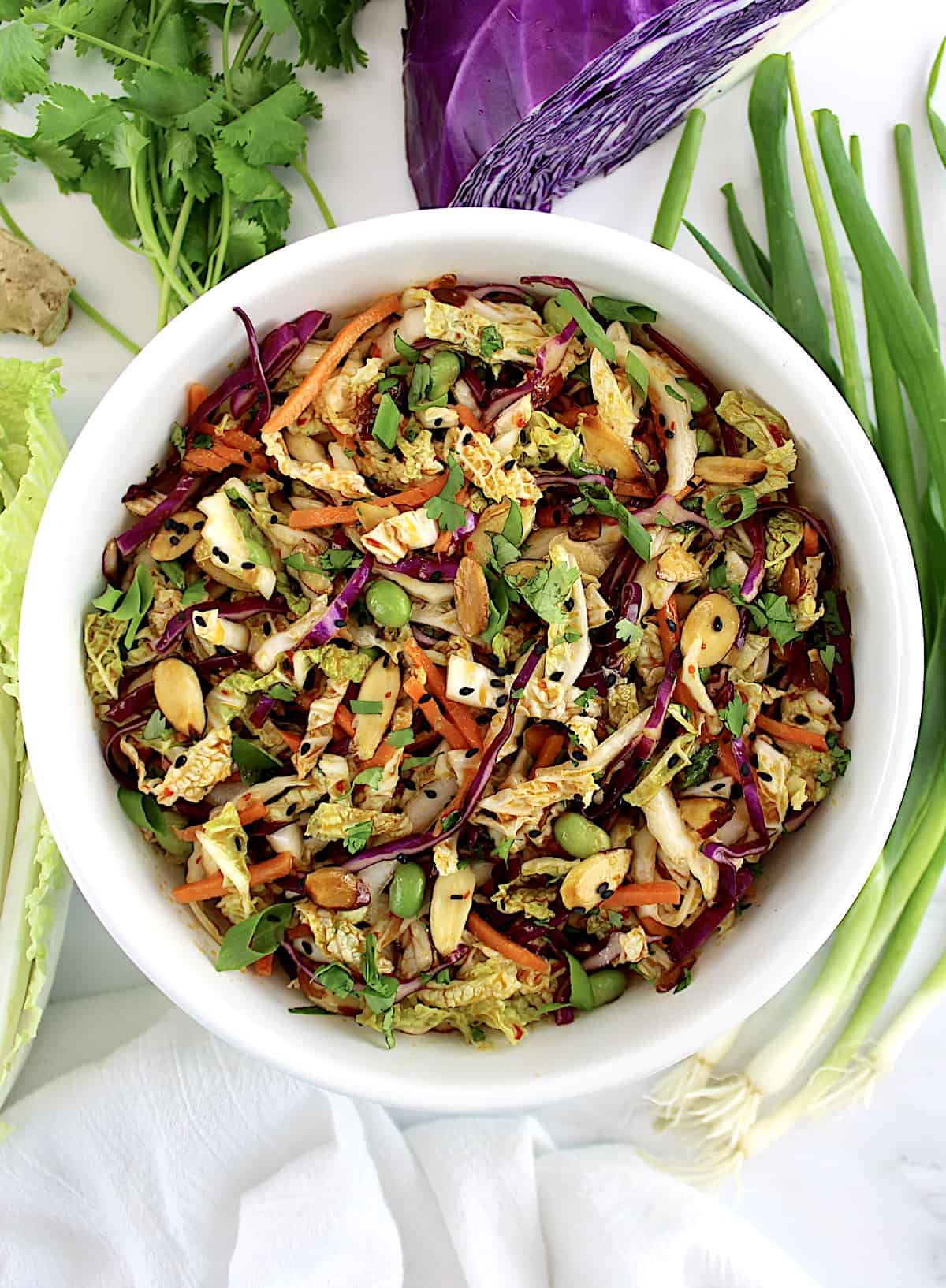 Asian Cabbage Slaw in white bowl with cabbage and scallions on side