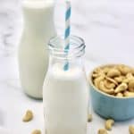 Cashew Milk in glass bottle with cashews in teal cup on side