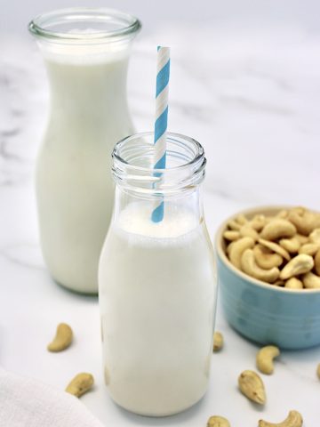 Cashew Milk in glass bottle with cashews in teal cup on side