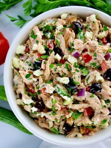 overhead view of Greek Salmon Salad in white bowl with veggies in background