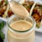 Yum Yum Sauce dripping off spoon into a jar with shrimp tacos in background