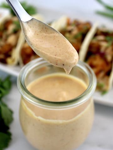 Yum Yum Sauce dripping off spoon into a jar with shrimp tacos in background
