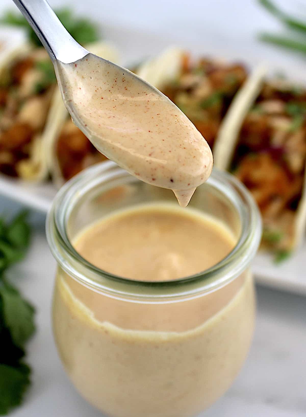 Yum Yum Sauce dripping off spoon into a jar with shrimp tacos in background