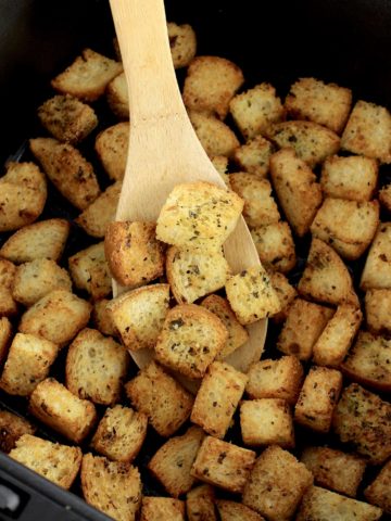 Air Fryer Croutons inn air fryer basket with wooden spoon