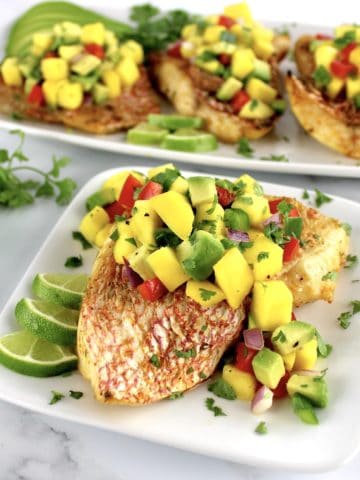 Broiled Red Snapper with Mango Salsa on top on white plate with more in background