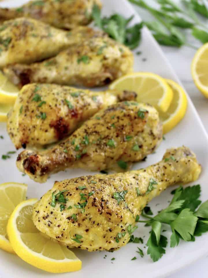 Lemon Pepper Baked Chicken Drumsticks on white plate with parsley and lemon slices