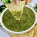 Salsa Verde in white bowl with tortilla chip being dipped in