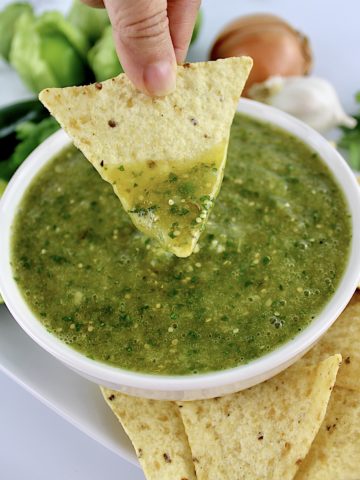 Salsa Verde in white bowl with tortilla chip being dipped in