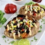 vegan black bean stuffed sweet potatoes with chipotle drizzle on top and lime slices on side